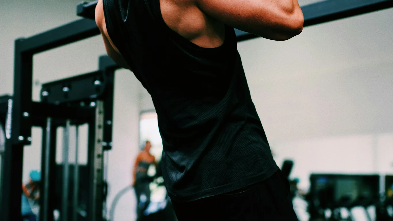 Mann beim Klimmzug an der Stange, Rückenansicht im Fitnessstudio