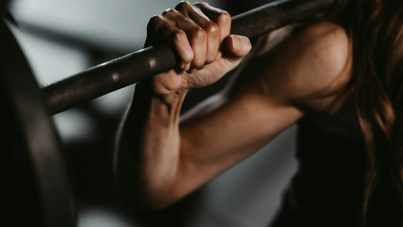 Junge Frau steht selbstbewusst am Squat Rack mit leicht beladener Langhantel