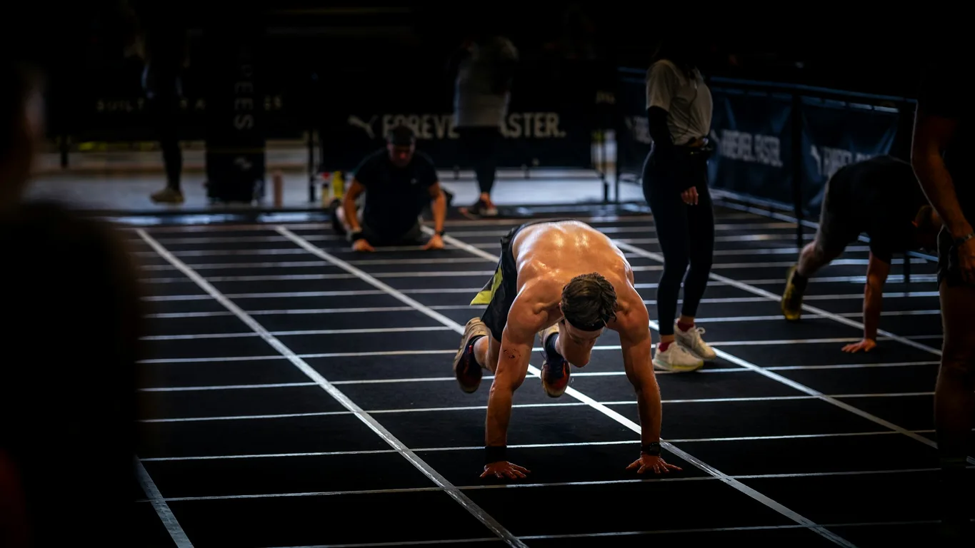 Weite Ansicht einer Functional-Fitness-Halle mit Athletin beim Sled Push auf Kunstrasen