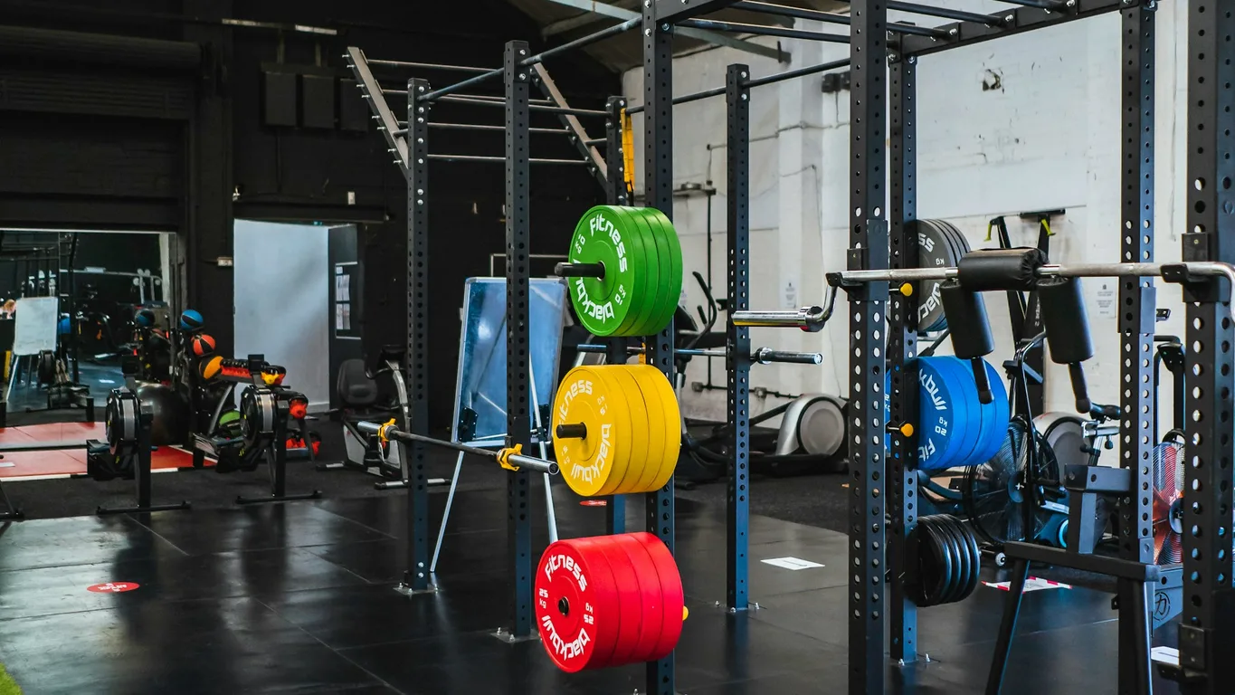 Aufgeschlagenes Trainingslog mit Stift auf einer Gym-Bank, Handschuhe und Flasche daneben