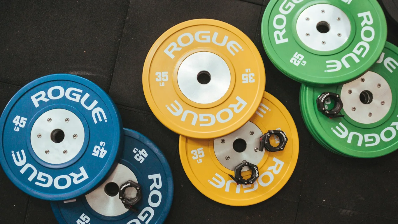 Kleine Gewichtsscheiben aufsteigend aufgereiht auf Gym-Boden, Langhantel unscharf dahinter
