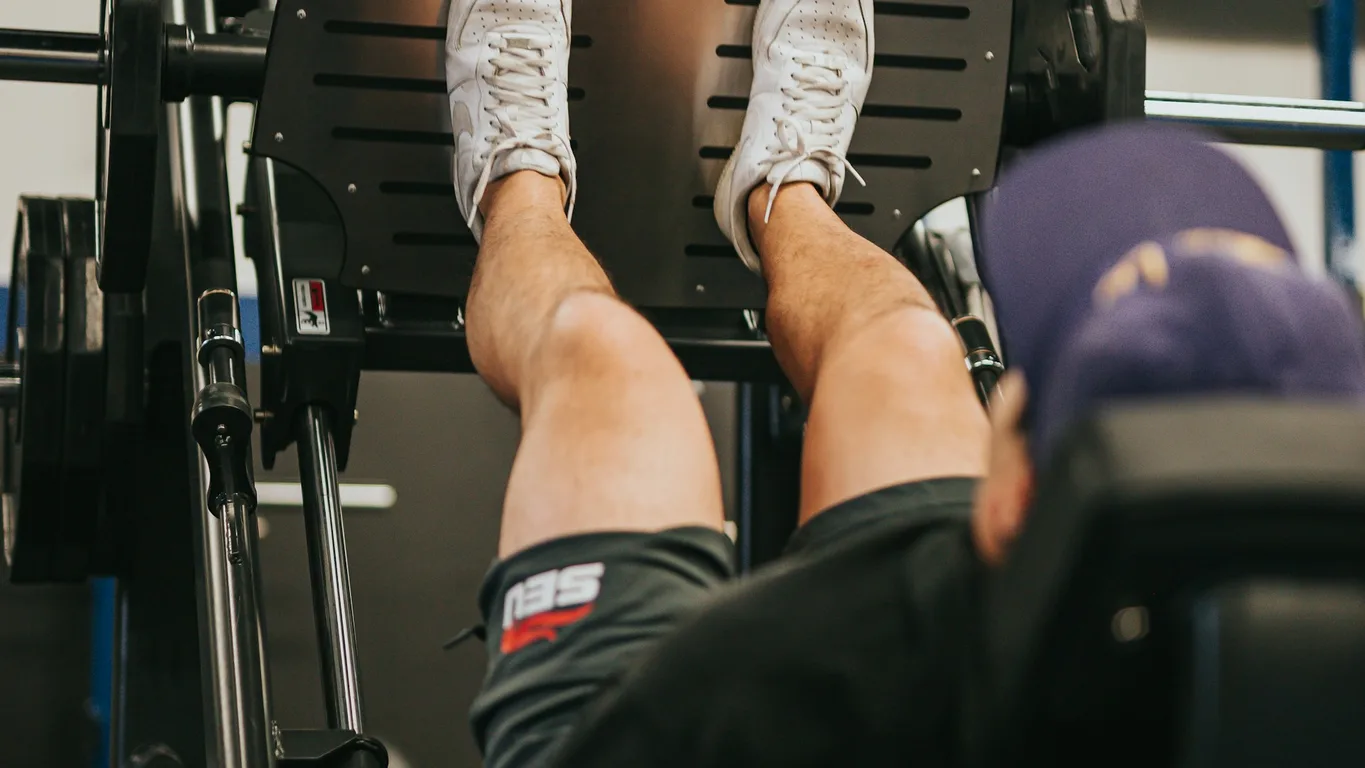Frau beim stehenden Kurzhantel-Schulterdrücken von hinten im Fitnessstudio
