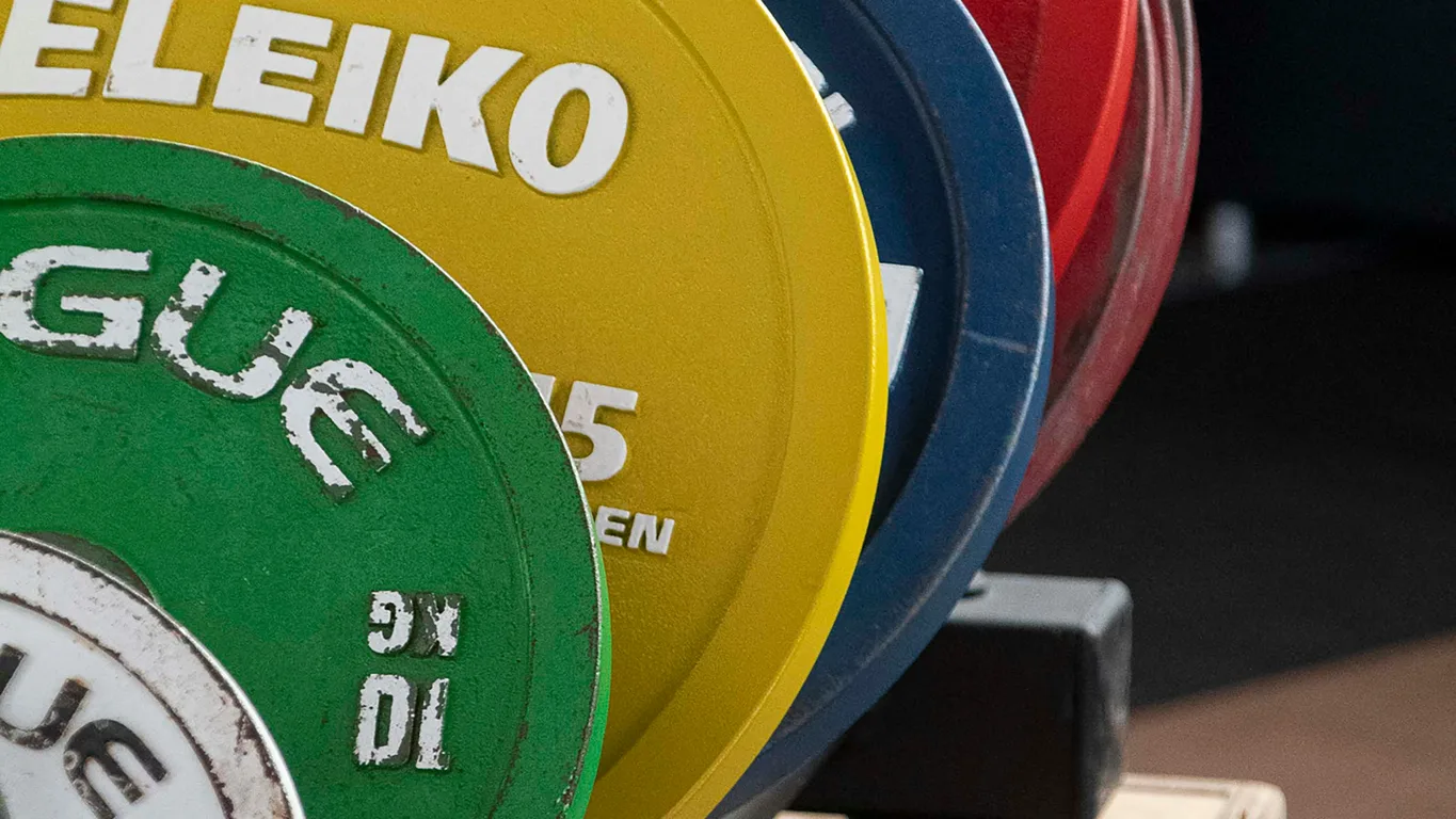 Mann sitzt auf Gym-Bank und schaut auf sein Smartphone, Gym im warmen Bokeh davor