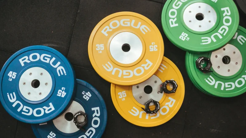 Kleine Gewichtsscheiben aufsteigend aufgereiht auf Gym-Boden, Langhantel unscharf dahinter
