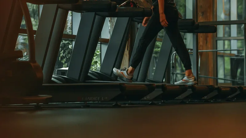 Person auf einem Laufband neben weiteren Laufbändern im Fitnessstudio.