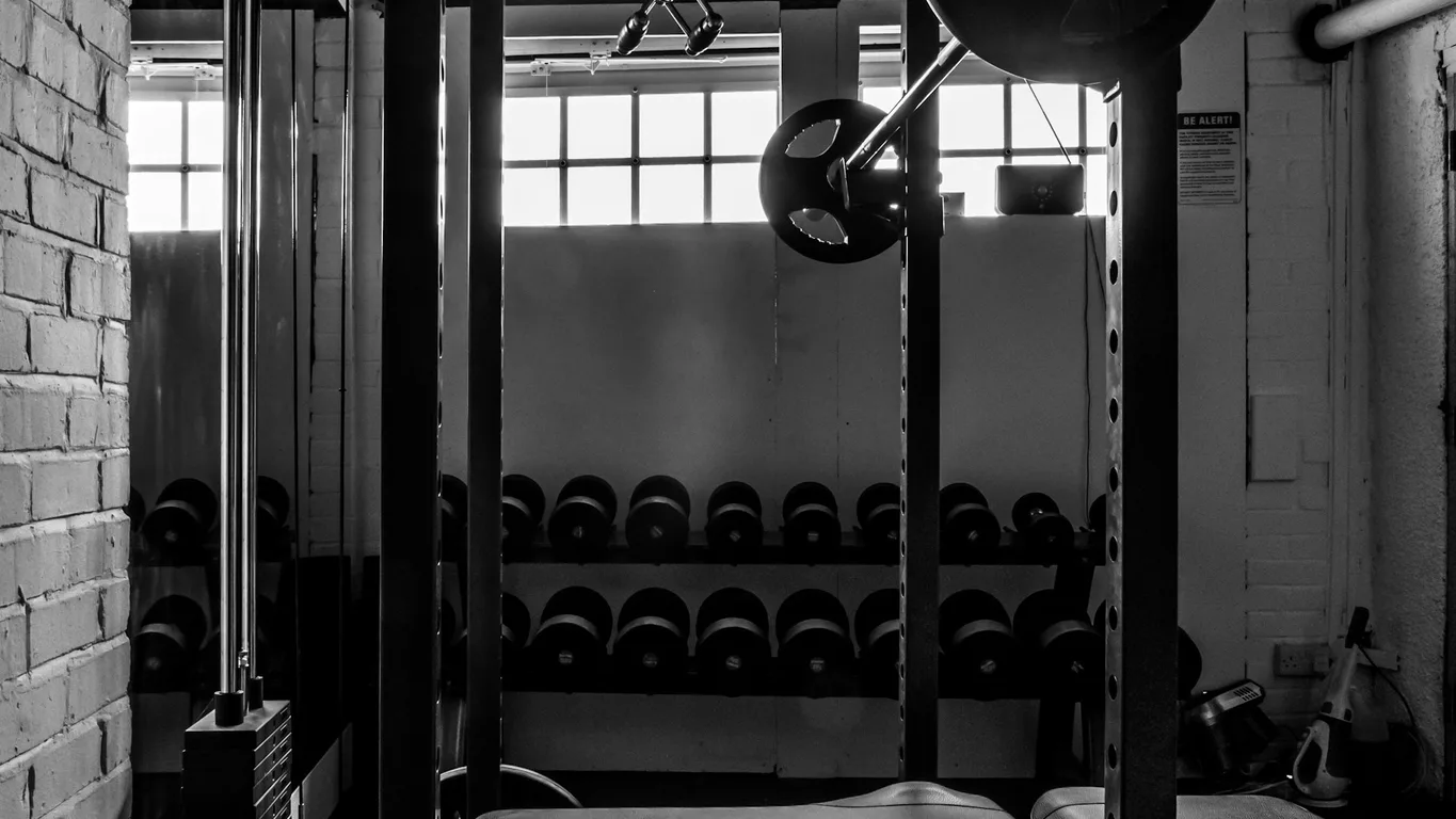 Mann steht nachdenklich vor einem Squat Rack, Rückansicht, warmes Licht